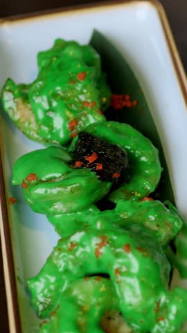 Fork pressing green glazed shrimp bite on rectangular dish crispy coating under glossy sauce, chili flakes sprinkle, closeup motion of tasting action, street food energy and playful foodie moment