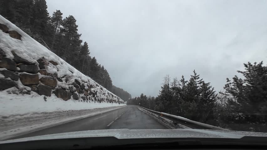 Point of view from a car driving on a curvy mountain road surrounded by a snowy pine tree forest