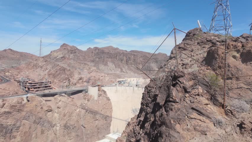 A moving shot revealing the Hoover Dam from behind the rocky surroundings.