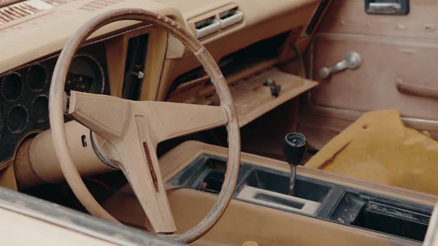 Dusty, abandoned car interior in Morocco. The steering wheel and dashboard show signs of age and decay. The seats are torn. This evokes a sense of nostalgia, history, and forgotten journeys.