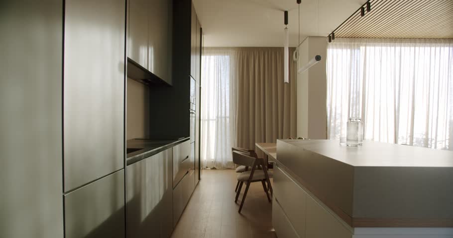 Modern kitchen interior with minimalist design, featuring an island and dining area. Stylish cabinets and contemporary lighting create a luxurious atmosphere.
