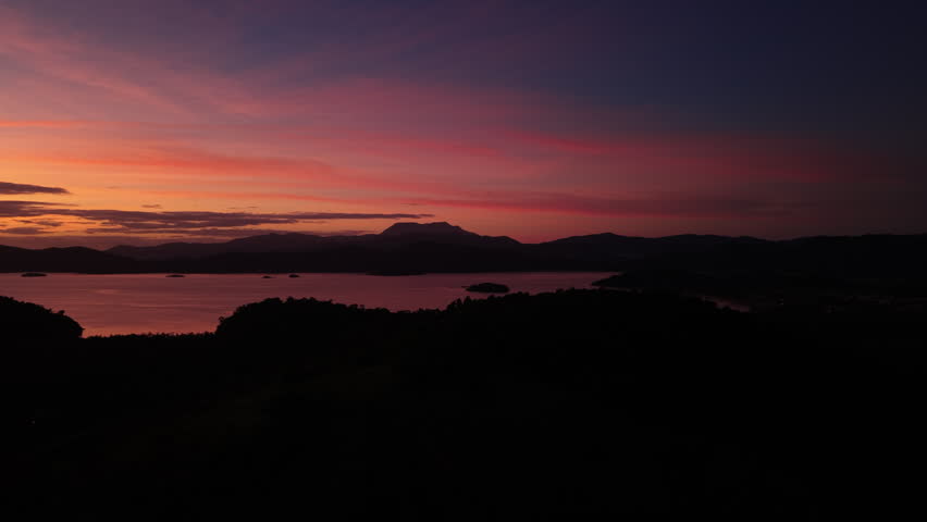 A dramatic wide view of a vibrant orange sunset sky above a tropical coastline with island silhouettes