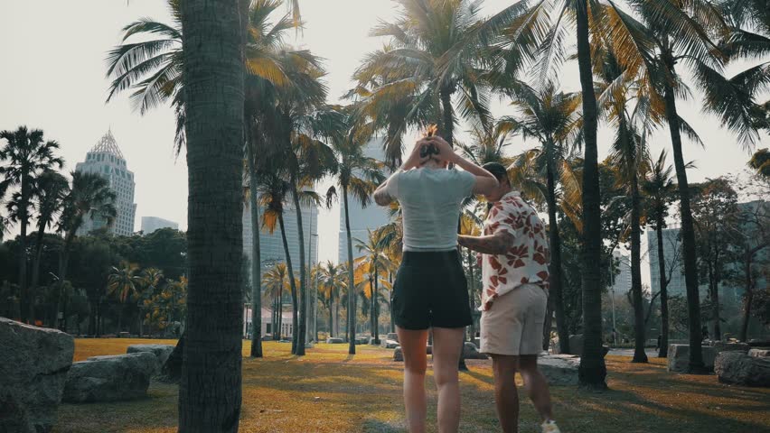 Young couple walking in a park in Bangkok with skyscrapers in the background.