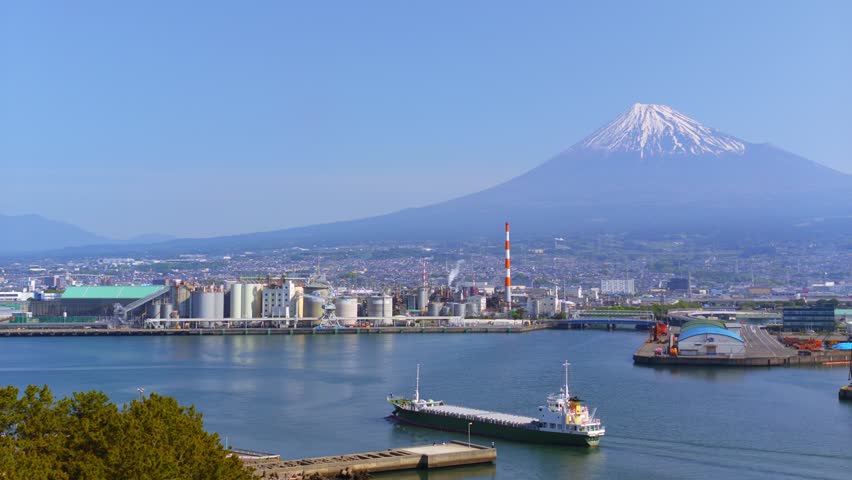 Horizontal panning shot to the right showing Mount Fuji and Tagonoura Port with a moving ship in Shizuoka, Japan.