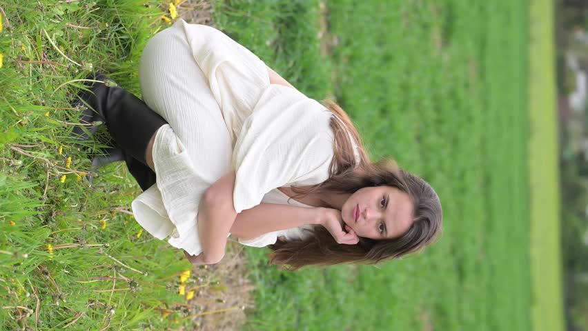 Thoughtful young woman crouching in green field, emotional outdoor portrait with soft countryside mood.
