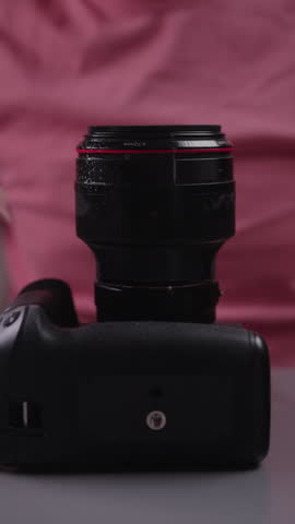 Professional videographer cleaning camera lens with spray cleaner and microfiber cloth before photo session, maintaining photographic equipment for optimal quality. Shooting in slow motion.