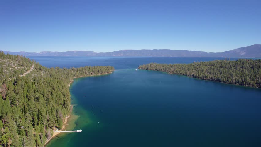 Drone footage capturing a calm bay opening into a vast lake surrounded by forested terrain.