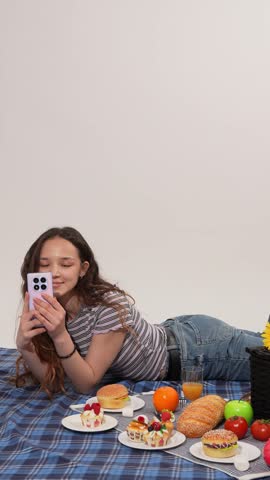 Young woman lying on picnic blanket and waving hand to camera