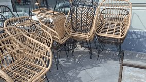 Multiple contemporary wicker armchairs with black metal legs outside shop or cafe. Rows of stacked decorative rattan chairs natural tones waiting on sidewalk. Furniture retail or cozy terrace styling - Powered by Shutterstock - Get 15% off with code: PIKWIZARD15