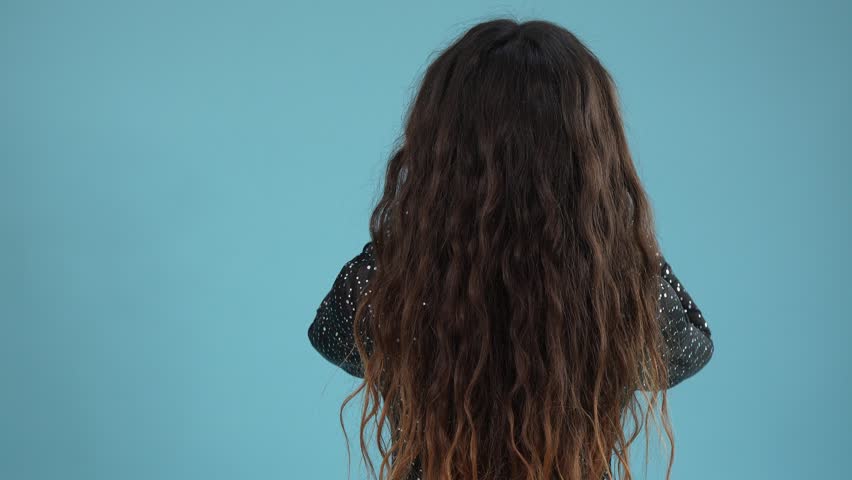 Back view of a woman with long curly hair touching her head