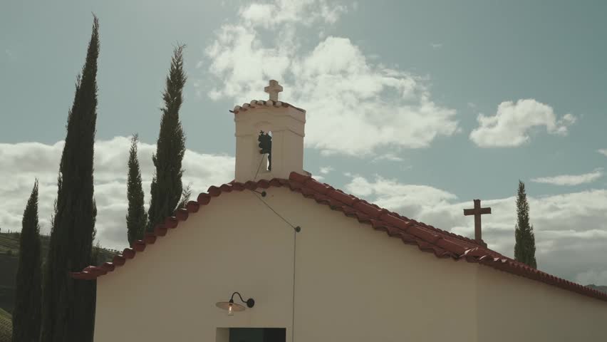 Small white chapel with bell tower and crosses rises among cypress trees in Douro