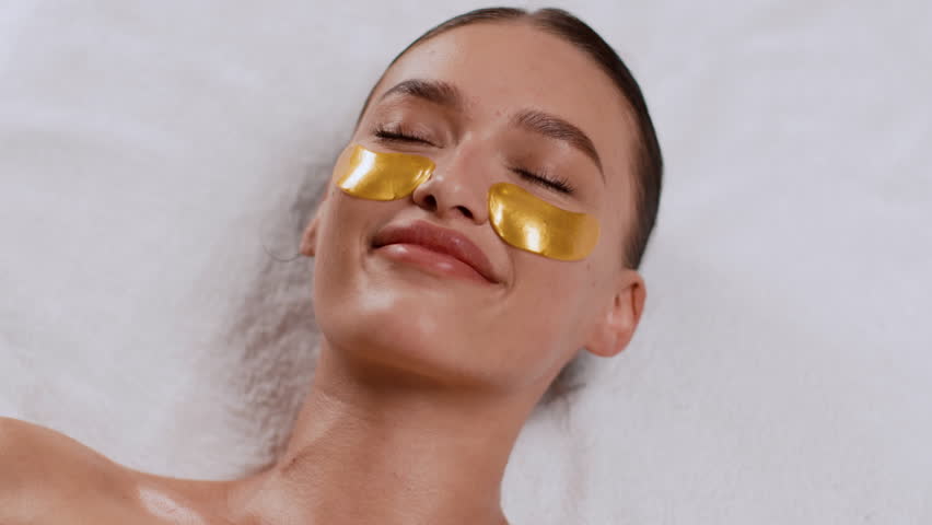 Woman Relaxing With Gold Under-Eye Patches During Facial Treatment in Spa Setting
