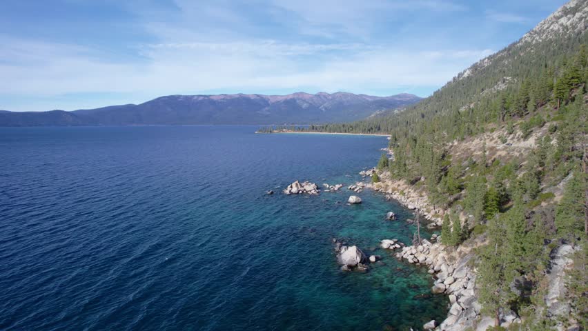 Scenic aerial of rocky shoreline with evergreen forest and clear lake water