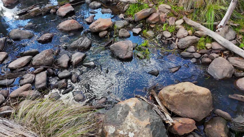 Static high angle shot of a clear creek flowing over smooth rocks in the outback