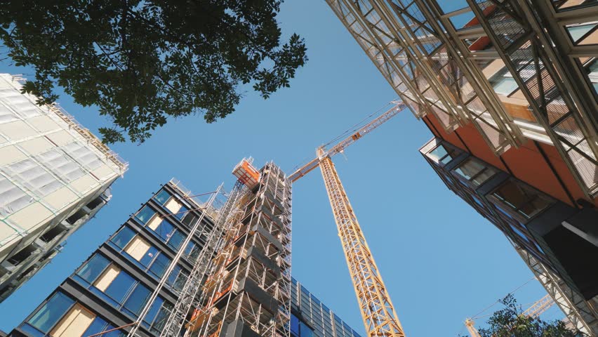 Construction crane moving against blue sky in an urban setting.