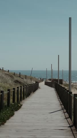 Wooden walkway through dunes leading toward ocean under clear sky