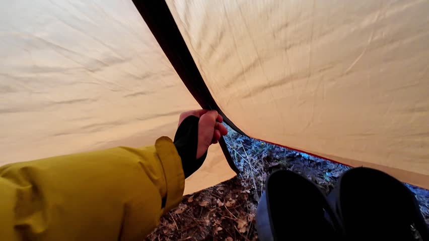 View from tent camping riverside, domestic campsite scene with clothesline drying jacket and socks above grassy bank at dusk, tent opening framing tranquil river valley and evening routine.