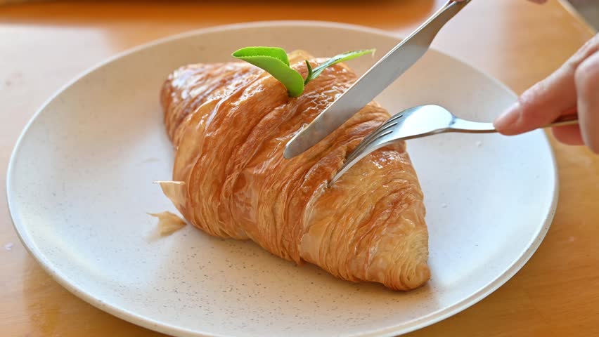 Someone cutting a piece of Matcha (or green tea) croissant for eating. Croissant is a French buttery, flaky and crescent-shaped bread.