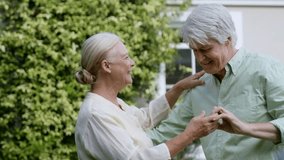 Lifestyle senior couple dancing in garden, woman placing hand starting confetti and showing joy. Outdoor, daylight, yard, hedge, duo, affection, romance - Powered by Shutterstock - Get 15% off with code: PIKWIZARD15