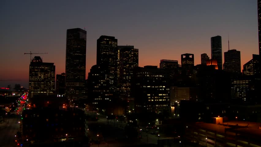Cinematic aerial view of Houston Texas city center at twilight. Urban landscape with glowing office windows and dark buildings against sunset sky. Motion footage of southern metropolis at night.