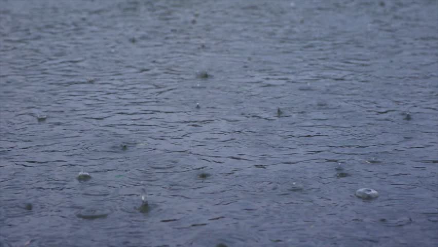 Raindrops falling on water surface creating ripples and splashes