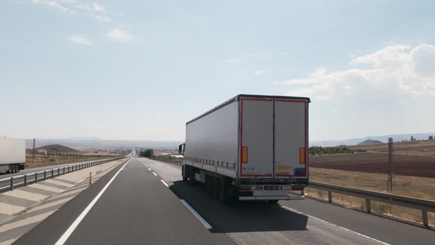 Cargo truck with a white semi-trailer is driving on highway in mountainous country