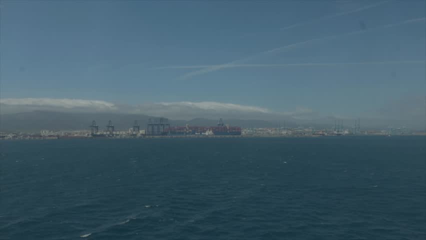 Distant view of Algeciras industrial port with cargo cranes and container ships seen from boat across blue Mediterranean sea