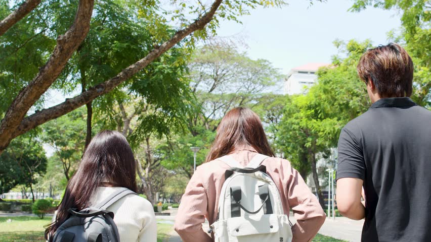 Back view of three students walking outdoors through a lush green university campus in Thailand
