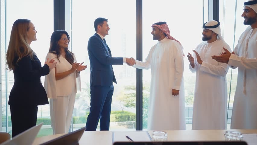 Corporate business event with emirati and western business people diverse business team, including arab men, smiling and shaking hands to seal an international deal