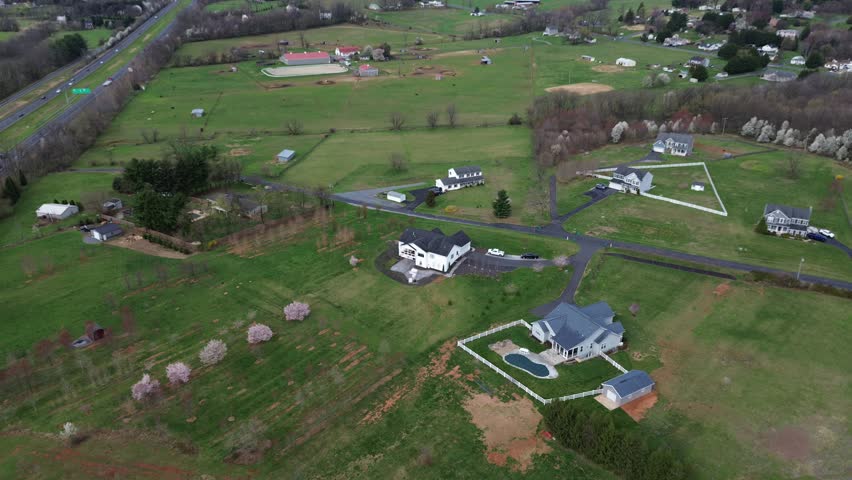 Highway agricultural sweep along US15 near Elmer Derr Rd with broad fields, flowering tree clusters, scattered buildings marking rural edge west of Frederick, mixed soil textures, Maryland. USA