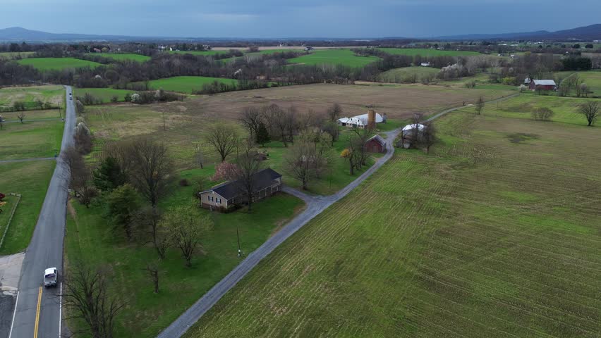 Farmstead ridge approach along Elmer Derr Rd near US15 with open fields, clustered barns, rolling terrain shaping western Frederick landscape shows muted roofing, soft tree canopies, Maryland. USA