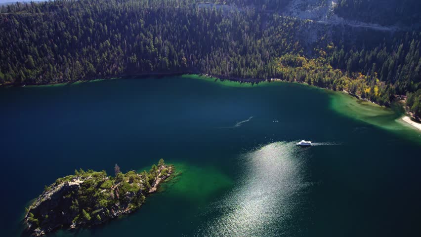 Cinematic aerial view of a mountain lake with a boat creating wake trails and sunlight reflecting on the surface.