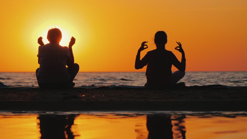 Two women meditating on beach at sunset, peaceful and tranquil scene.