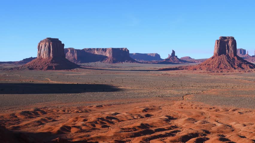 The iconic red sandstone buttes of Monument Valley. The valley is situated on the Colorado Plateau, straddling the border between Arizona and Utah within the Navajo Nation Reservation.These distinct rock formations are mesas and buttes, created over millions of years as erosion wore away layers of hard sandstone, leaving behind harder capstones that protect the softer rock beneath.