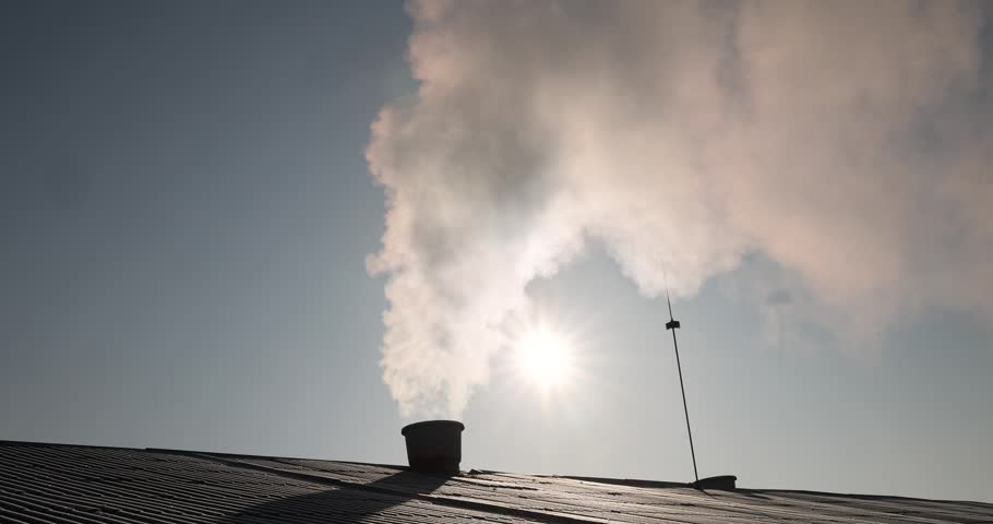 smoke coming from a wide pipe against a blue sky background, white steam coming from a pipe during heating of a large industrial premises in cold weather