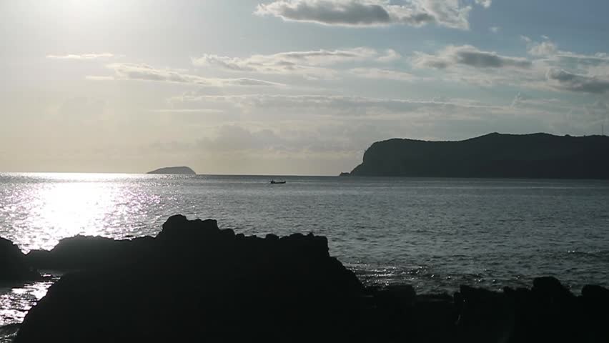 Silhouette of a boat in the middle of the sea with the sun shining brightly in the afternoon.