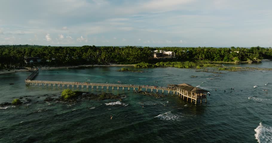 Wooden pier stretches into the ocean with surfers nearby. Cloud 9 Surfing Area. Siargao, Philippines.