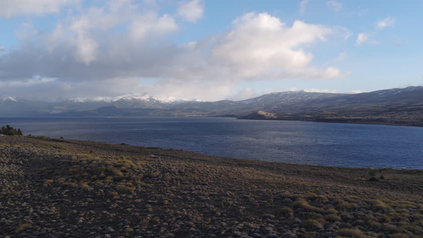 Clouds drift over Huechulafquen Lake with Lanin Volcano in the distance, capturing the rugged beauty of Patagonia. Ideal for travel content or nature documentaries.