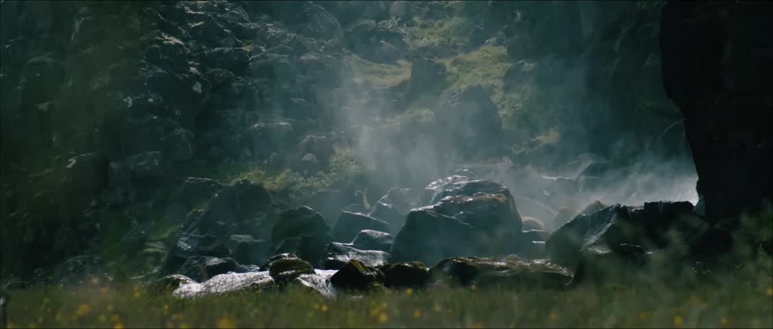 A beautiful natural scene of mist drifting over a rocky mountain stream in a green meadow landscape.