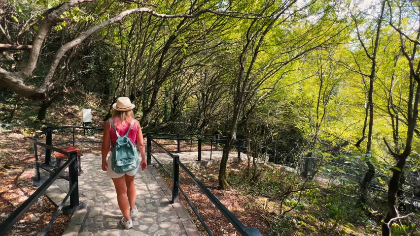 Young female traveler walking along the stone-paved Dadiani trail in the Lower Martvili Canyon surrounded by 40-meter limestone cliffs and lush Colchic greenery on a sunny day Georgia
