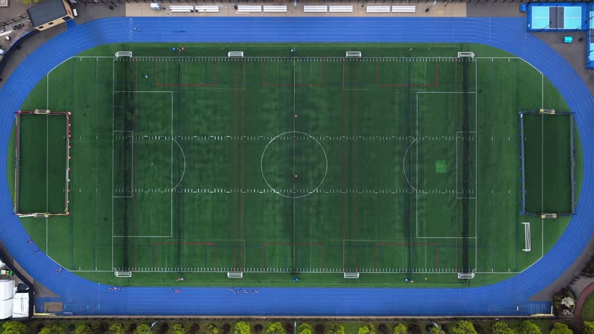 Flight above soccer stadium with blue running track encircling the artificial turf football field in a North America city