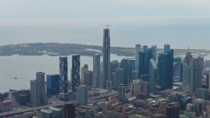 High altitude flight over downtown Toronto with clear shot of Lake Ontario and skyline featuring towering skyscraper under construction