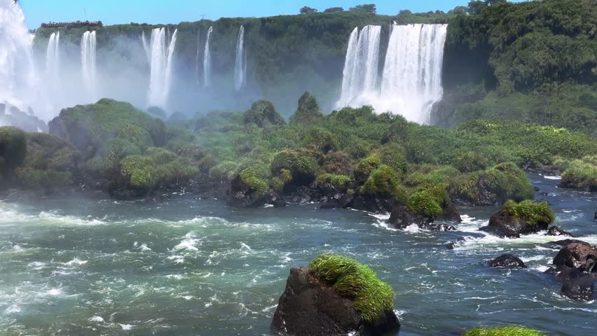 Panoramic view of the majestic Iguazu Falls in Foz do Iguacu, Brazil, showing powerful waterfalls cascading into the river surrounded by lush tropical rainforest vegetation
