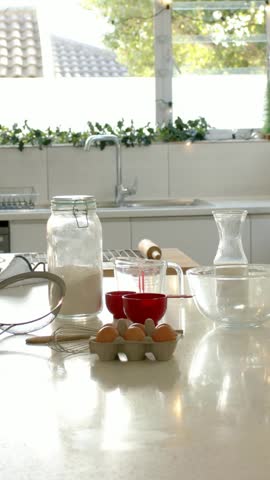 Vertical video: Panning camera revealing baking prep on home counter for baking, flour jar and eggs. Kitchen, countertop, mixingbowl, rollingpin, whisk, sieve, vertical video