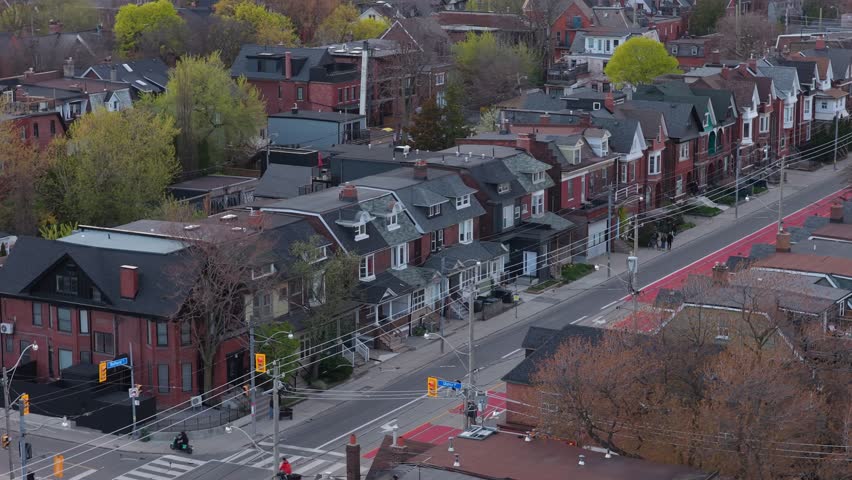 Flying over red streetcar lanes and residential houses in Toronto while cars and trams with people are moving on road during springtime