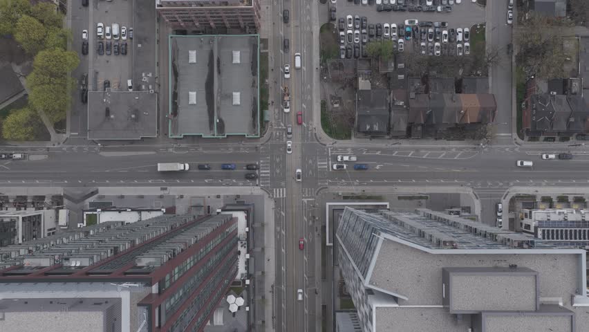 Top down shot of urban traffic at busy downtown area intersection with cars, pedestrians, cyclists navigating city streets alongside towering modern buildings