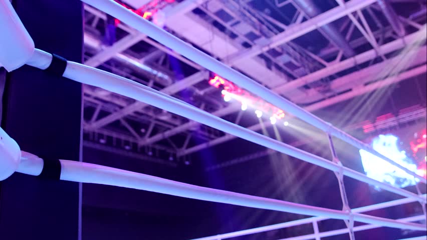 Close-up view of a boxing ring corner with ropes under bright arena lights during a professional sports event indoors.