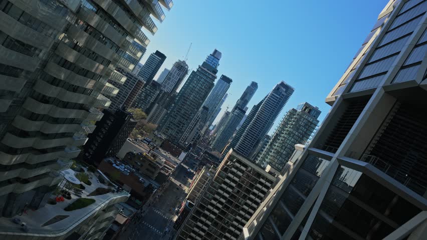 Cinematic descending between glass skyscrapers in Toronto, Canada, revealing downtown streets and city life below, clear blue sky reflecting on windows