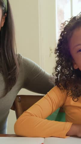 Vertical video: Reaching for red marker, child in orange top drawing at table with adult guiding. Kid, caregiver, bonding, encouragement, art, creativity, vertical video