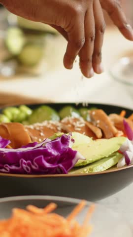 Vertical video: Entering hand adding seeds over poke bowl on counter, placing sauce cup, finishing. Closeup, colorful, vibrant, dish, avocado, cucumber, vertical video